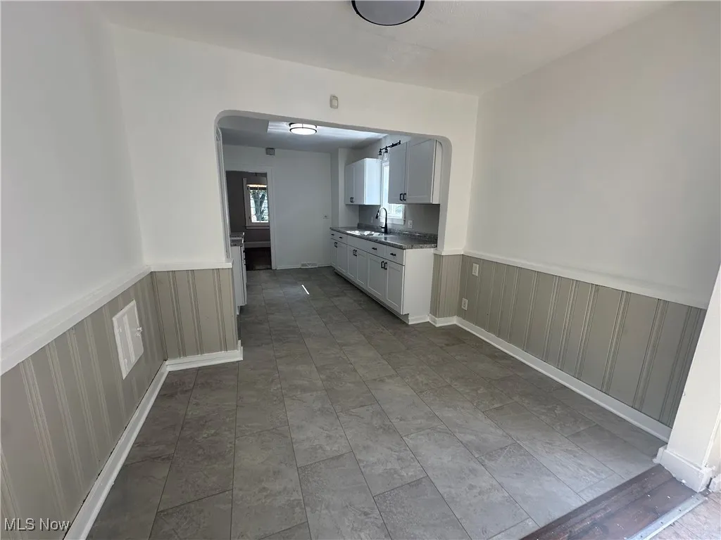 Kitchen featuring wainscoting, arched walkways, white cabinetry, and dark countertops