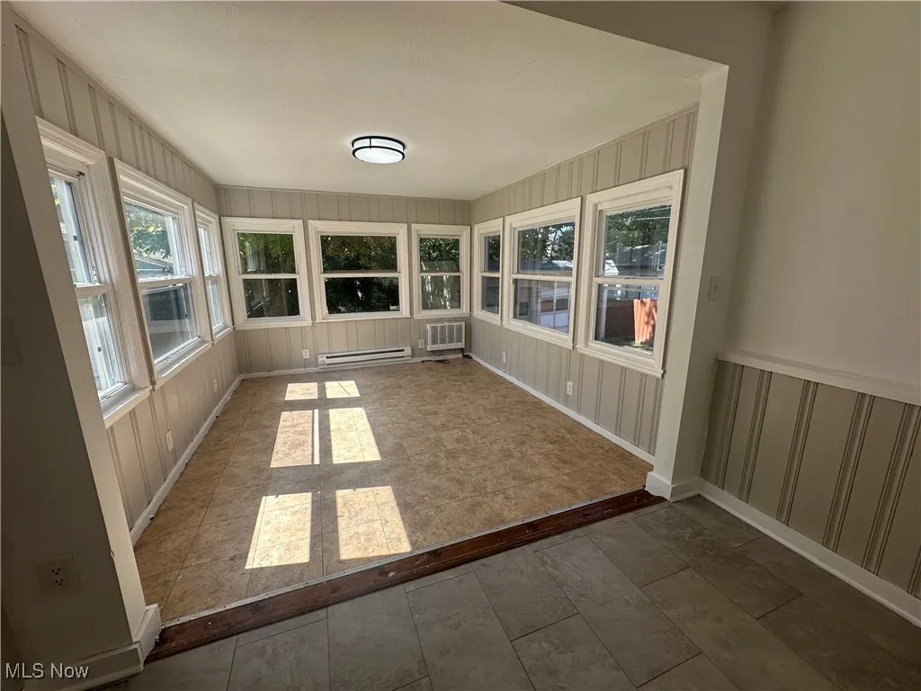 Unfurnished sunroom featuring plenty of natural light and a baseboard heating unit