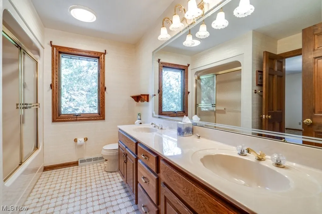 Full bathroom with bath / shower combo with glass door, plenty of natural light, and double vanity