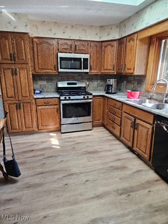 Kitchen featuring brown cabinetry, light wood-style flooring, stainless steel appliances, tasteful backsplash, and a textured ceiling