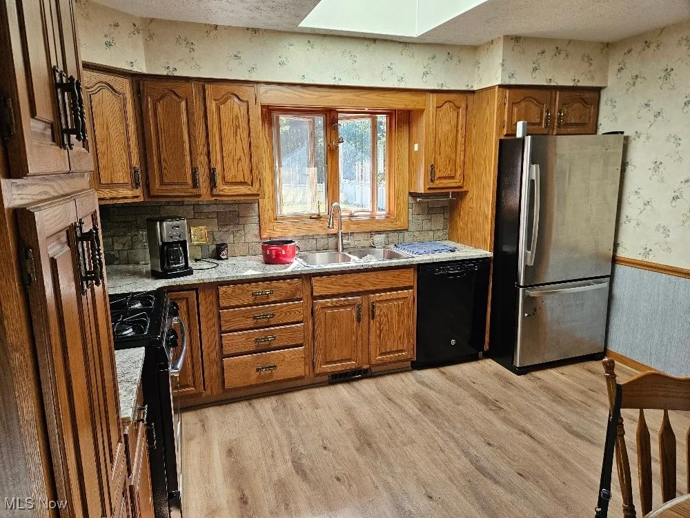 Kitchen featuring wallpapered walls, brown cabinetry, freestanding refrigerator, light wood finished floors, and dishwasher