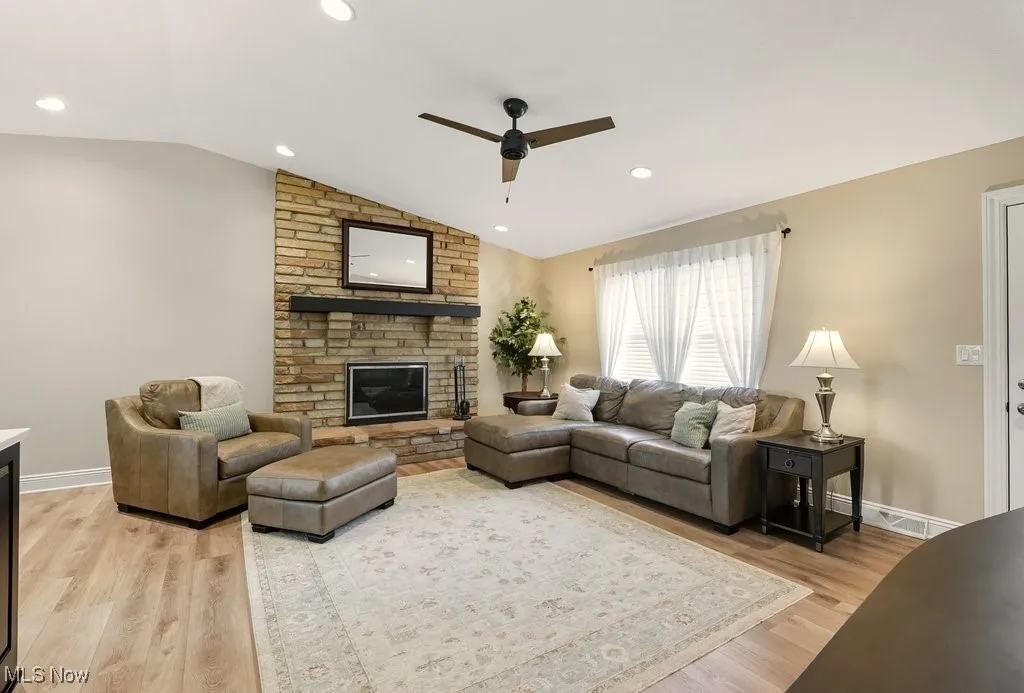 Living area with a fireplace, lofted ceiling, light wood finished floors, recessed lighting, and ceiling fan
