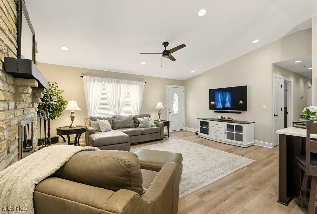Living room featuring light wood-type flooring, a fireplace, recessed lighting, vaulted ceiling, and ceiling fan