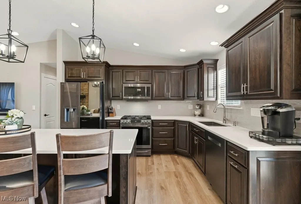 Kitchen with dark brown cabinets, decorative backsplash, lofted ceiling, stainless steel appliances, and light wood-style flooring