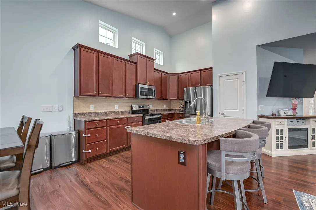 Kitchen featuring decorative backsplash, appliances with stainless steel finishes, dark wood-style flooring, a breakfast bar area, and a high ceiling