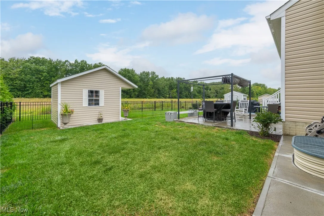 Fenced backyard with a patio, an outbuilding, and view of scattered trees