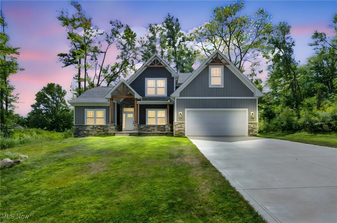 Craftsman inspired home with driveway, a garage, stone siding, a front yard, and board and batten siding