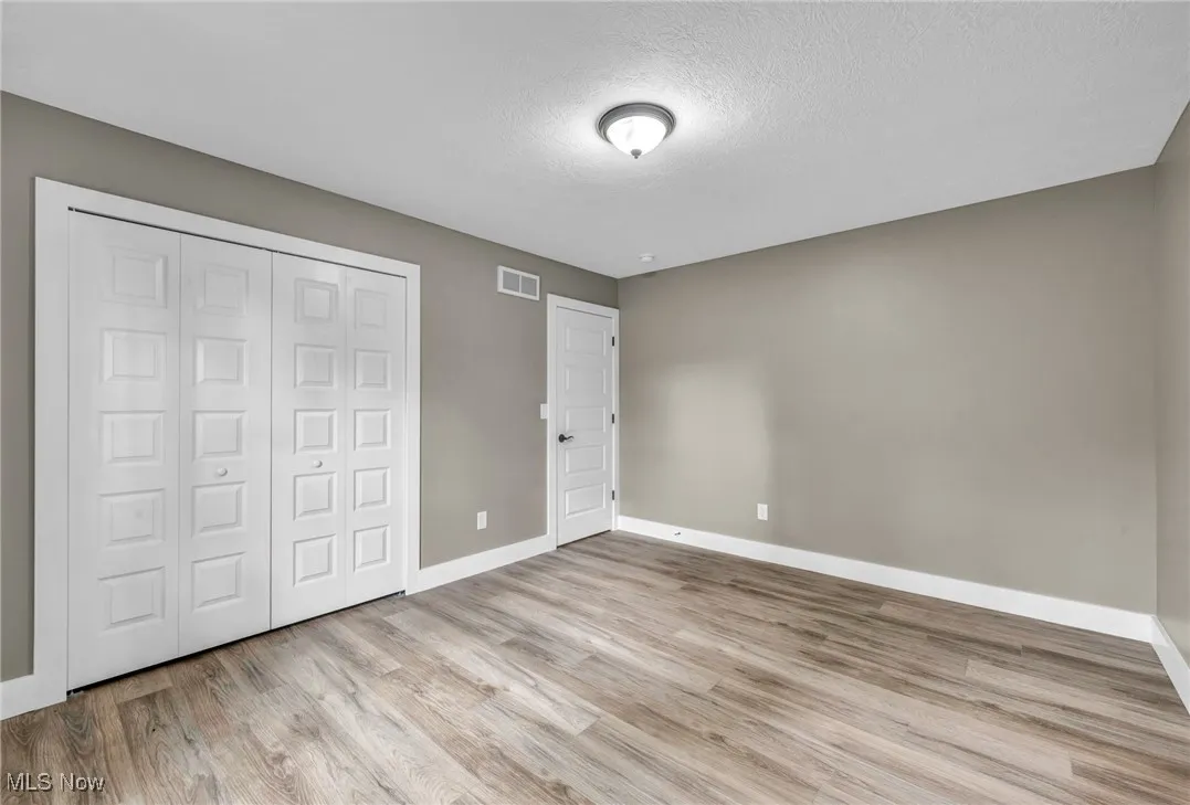Unfurnished bedroom with light wood-type flooring, a textured ceiling, and a closet