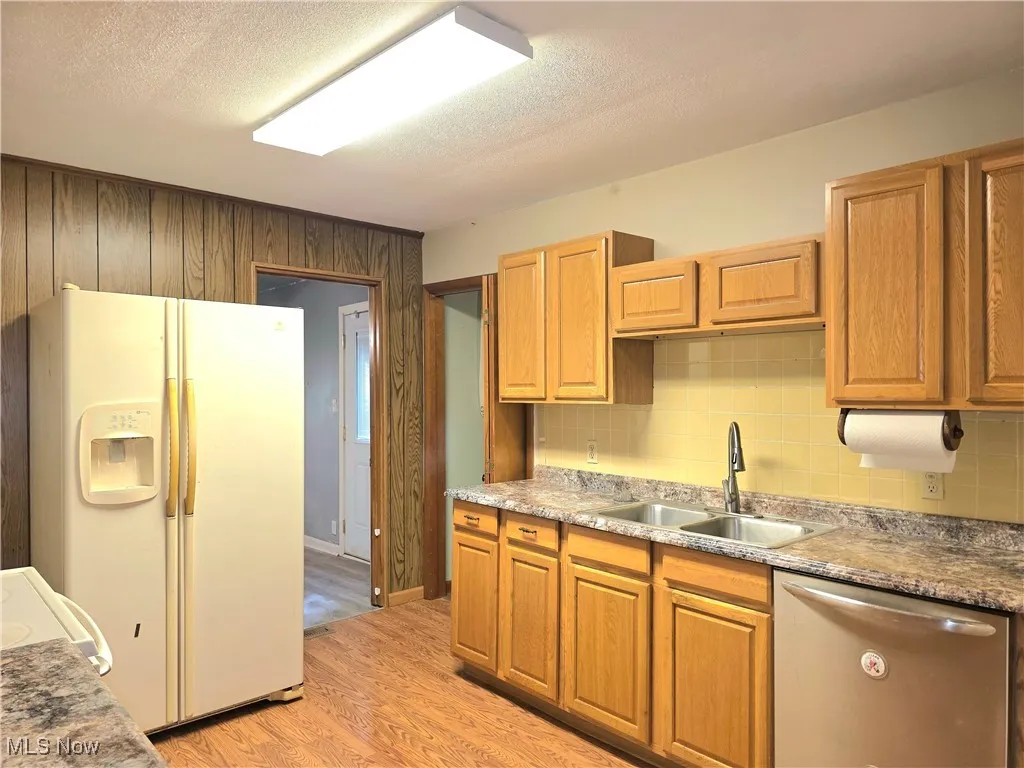 Kitchen featuring white appliances, light wood-style floors, backsplash, a textured ceiling, and wooden walls