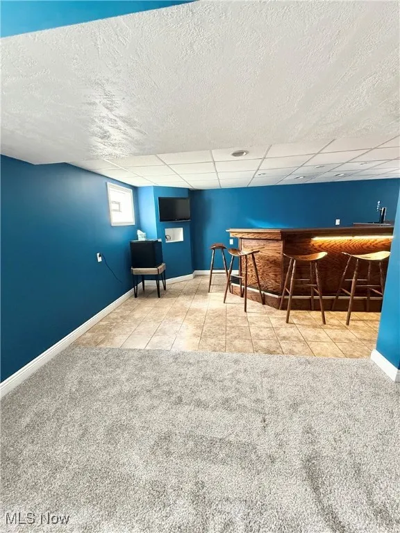 Indoor bar featuring light tile patterned floors, light carpet, and a drop ceiling
