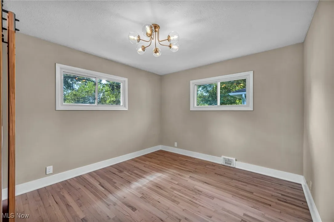 Unfurnished room featuring light wood finished floors, a chandelier, and a textured ceiling