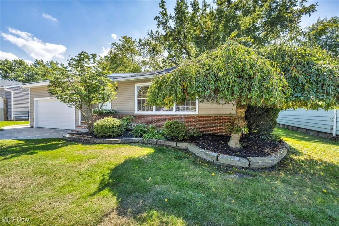 View of front facade featuring brick siding, asphalt driveway, a front yard, and a garage