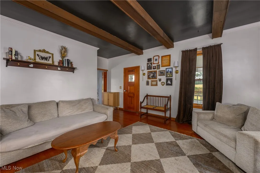 Living area with beamed ceiling, wood finished floors, and ornamental molding