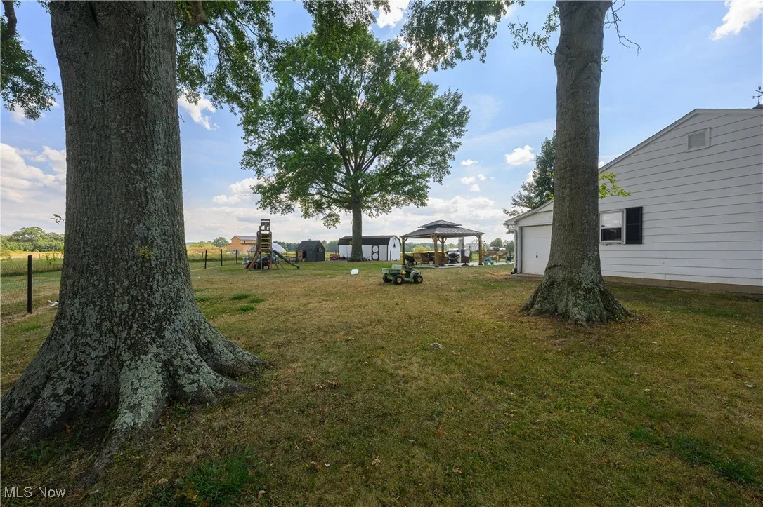 View of green lawn with a playground, a gazebo, and a garage