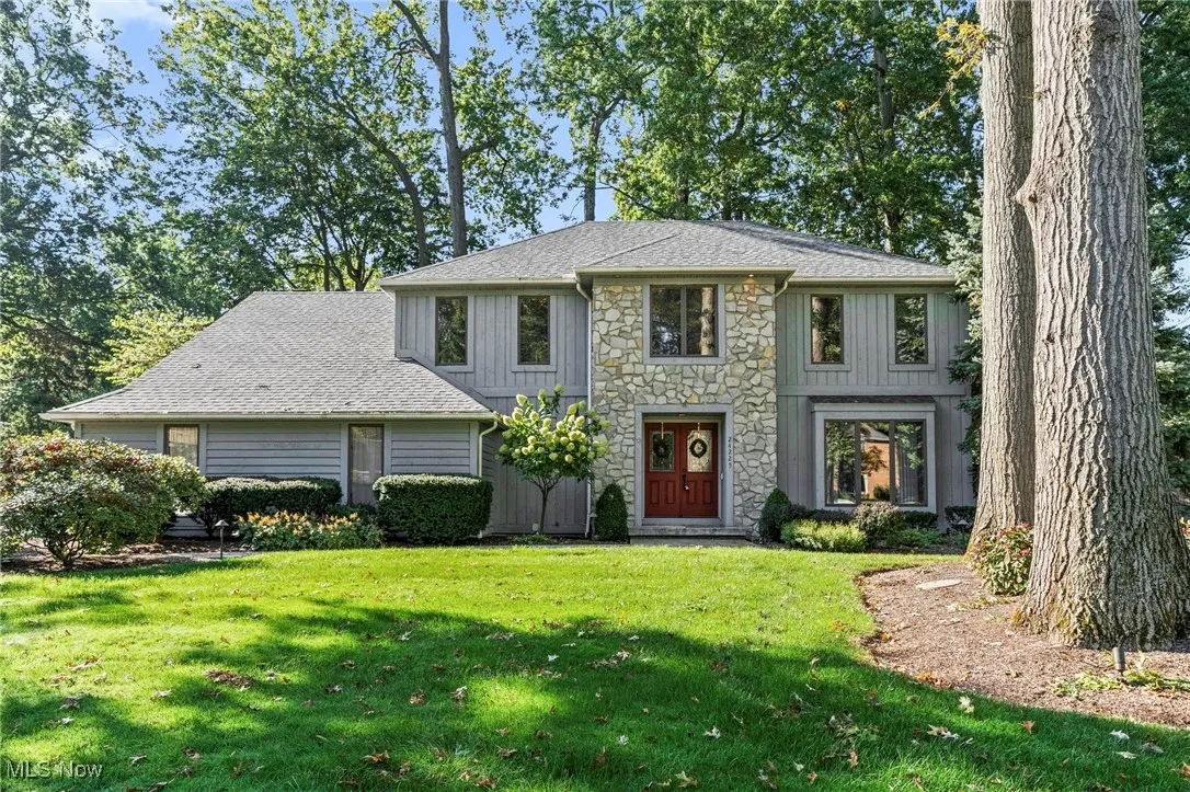 View of front of home with stone siding, roof with shingles, a front yard, and board and batten siding