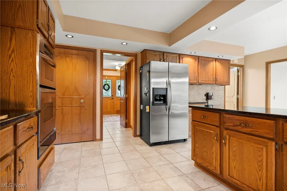 Kitchen with brown cabinets, appliances with stainless steel finishes, light tile patterned floors, recessed lighting, and tasteful backsplash