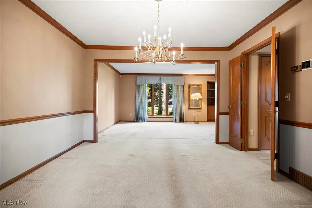 Carpeted empty room with crown molding and a chandelier