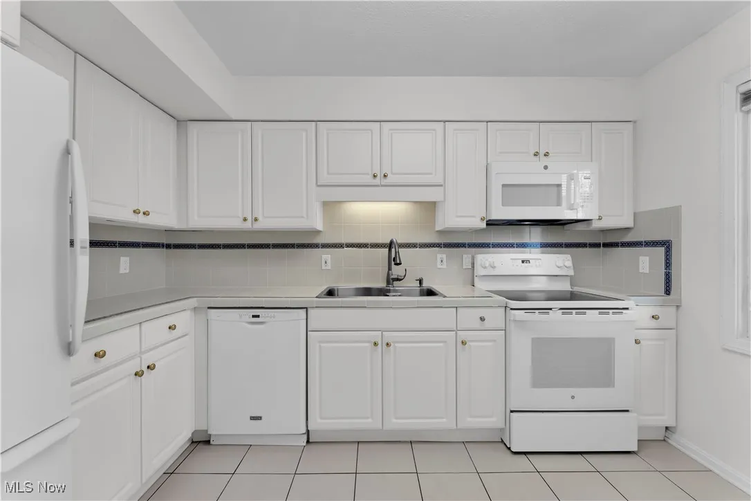 Kitchen with white appliances, white cabinetry, and tasteful backsplash