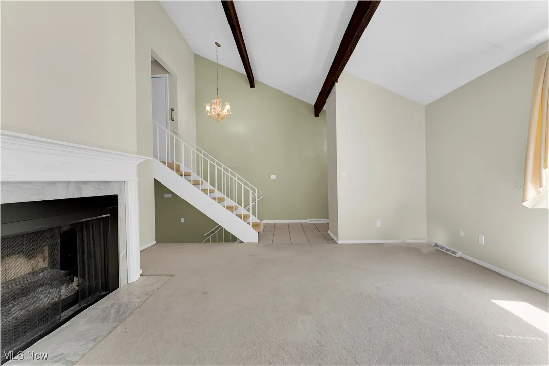 Unfurnished living room featuring a fireplace, beamed ceiling, carpet, a chandelier, and stairs