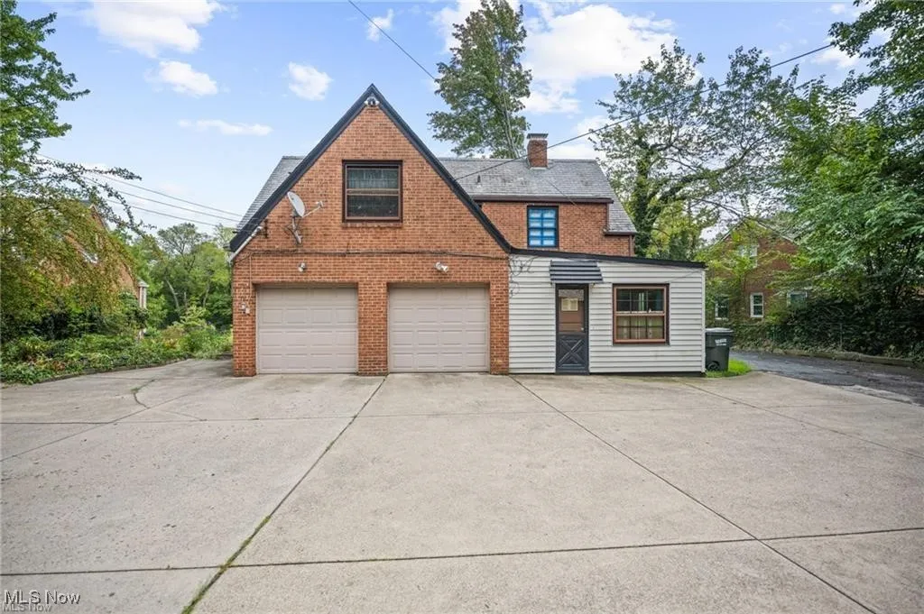 View of front facade with driveway, brick siding, and a chimney