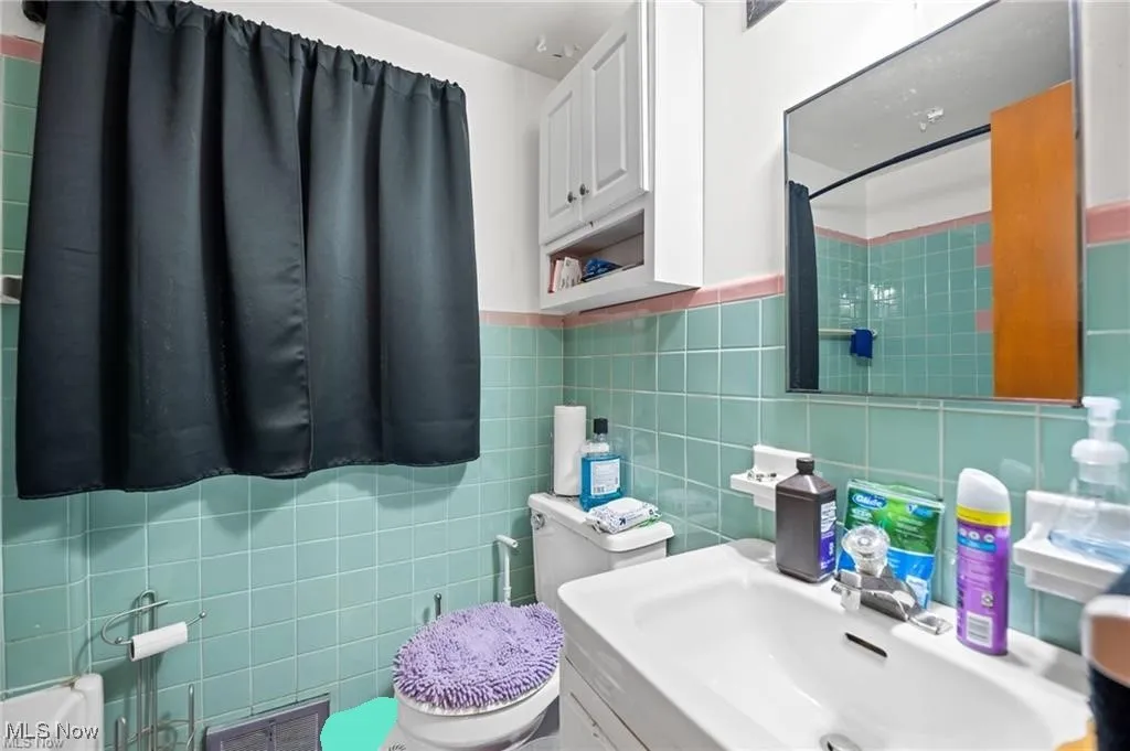 Bathroom with tile walls, a shower with shower curtain, and wainscoting