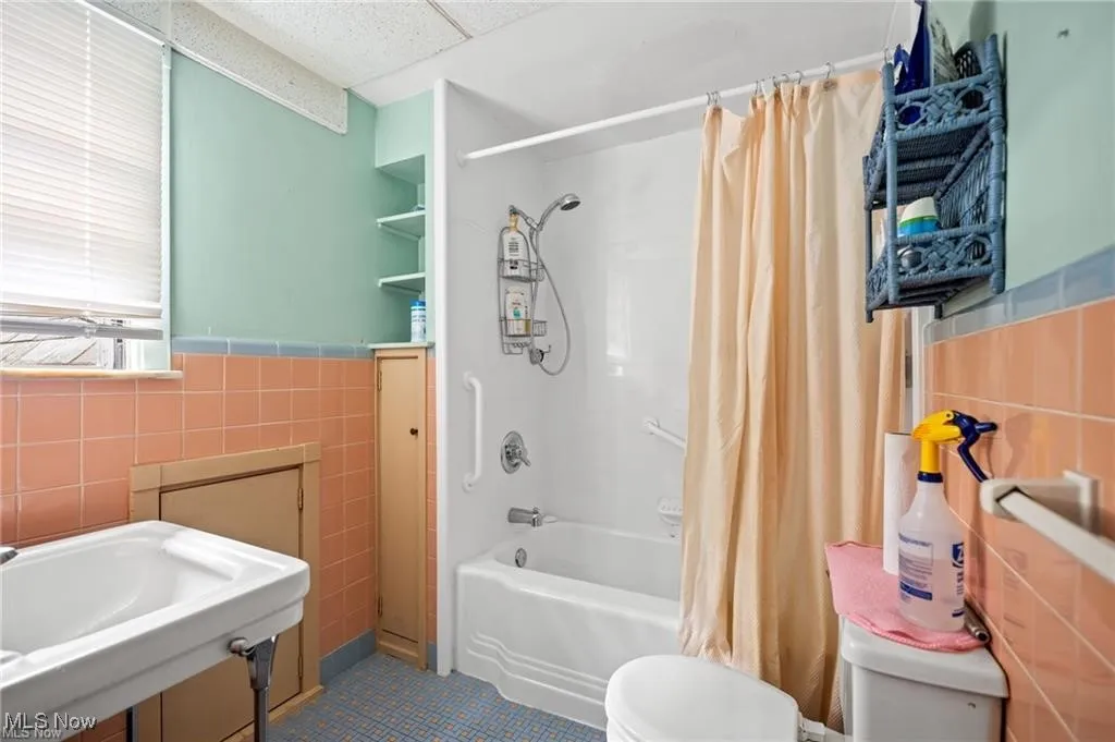 Bathroom featuring tile walls, shower / tub combo with curtain, wainscoting, a drop ceiling, and tile patterned floors