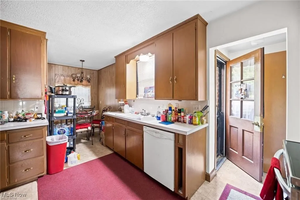 Kitchen featuring light countertops, white dishwasher, brown cabinets, a chandelier, and pendant lighting