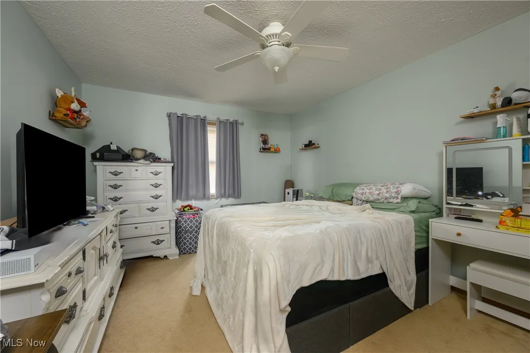 Bedroom with light colored carpet, a textured ceiling, and ceiling fan