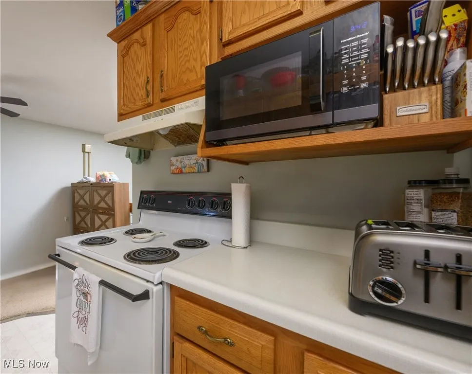Kitchen featuring brown cabinets, electric range, black microwave, and light countertops