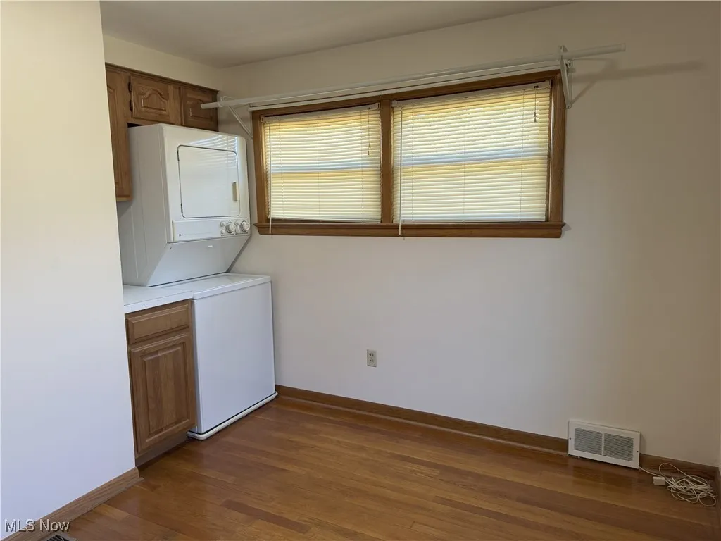 Washroom featuring dark wood-style flooring, stacked washer and clothes dryer, and cabinet space