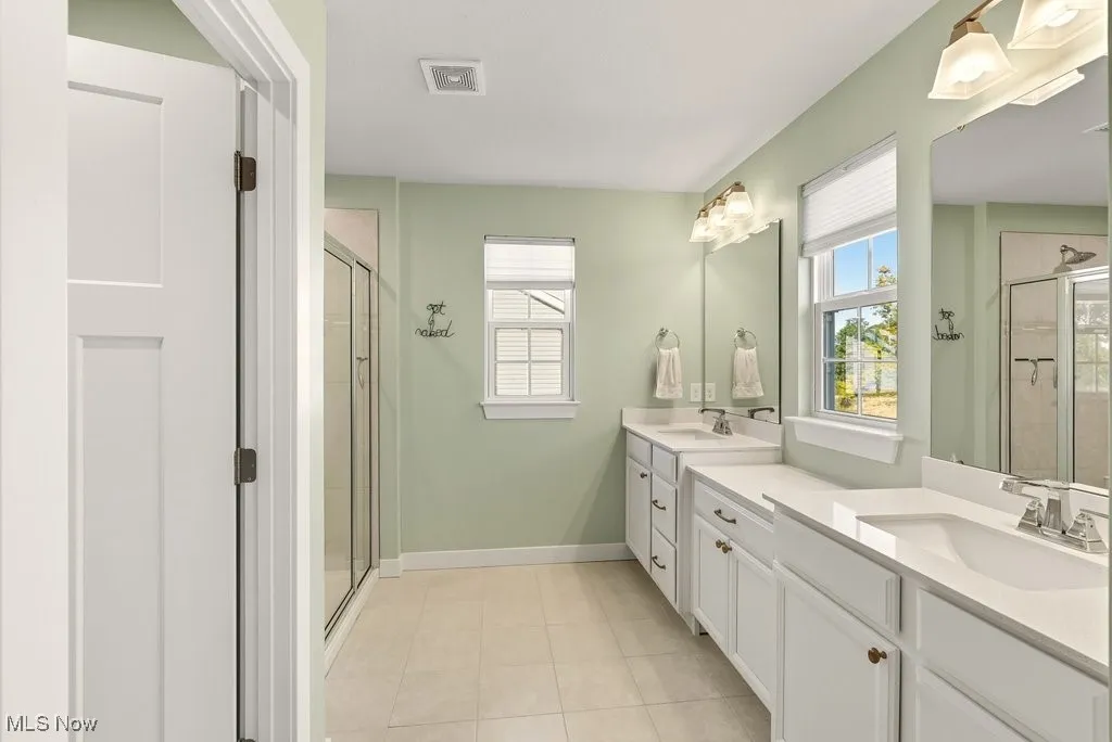 Full bathroom featuring a stall shower, two vanities, plenty of natural light, and light tile patterned flooring