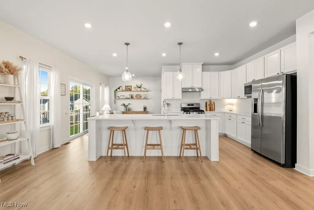Kitchen with appliances with stainless steel finishes, white cabinetry, decorative light fixtures, open shelves, and a kitchen breakfast bar