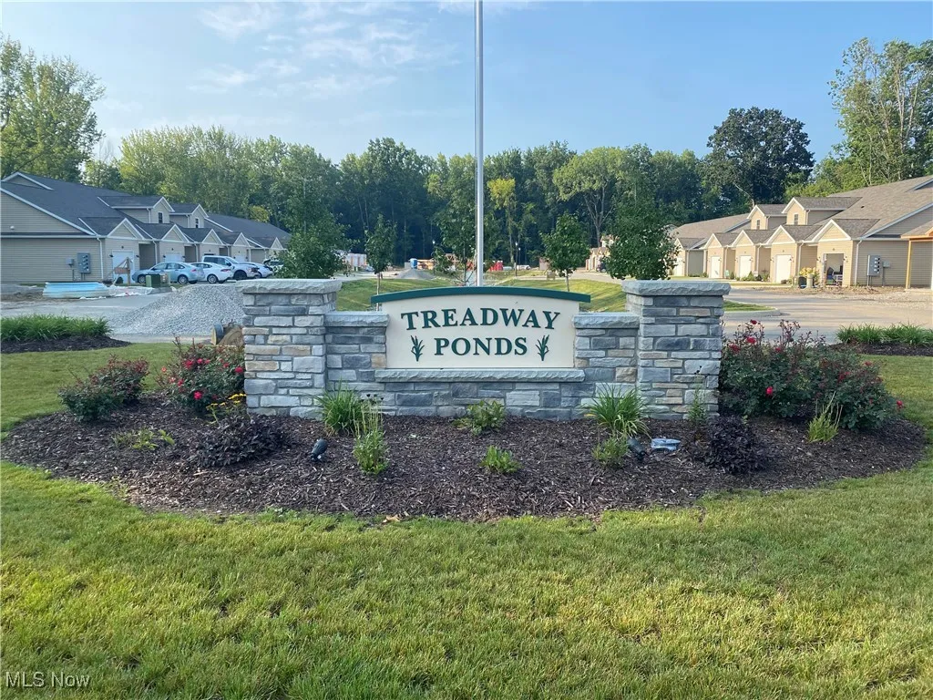 Community sign featuring a lawn and view of scattered trees