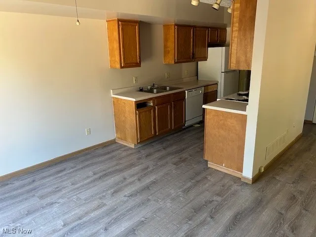 Kitchen with white appliances, light countertops, dark wood-type flooring, and brown cabinets