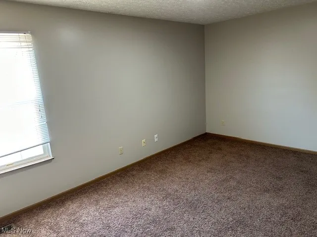 Carpeted empty room with a textured ceiling and baseboards
