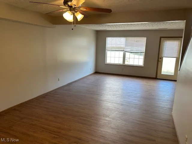 Empty room with a textured ceiling, wood-style finished floors, and a ceiling fan