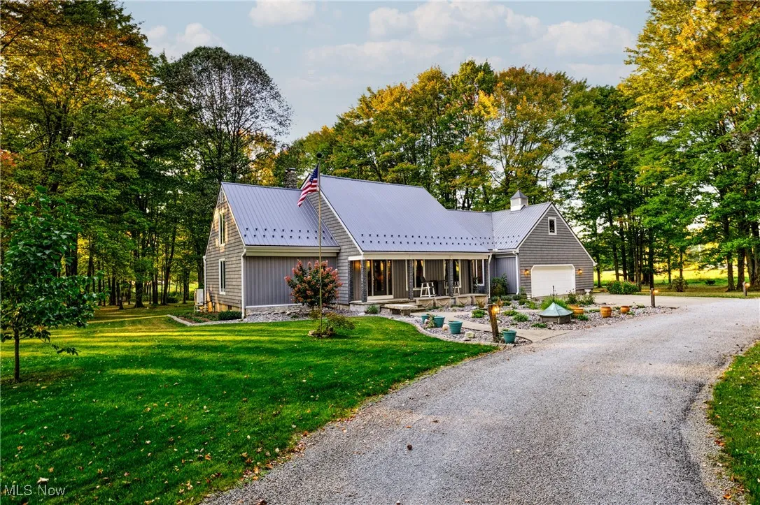 View of front facade featuring a porch, a front yard, view of scattered trees, driveway, and an attached garage