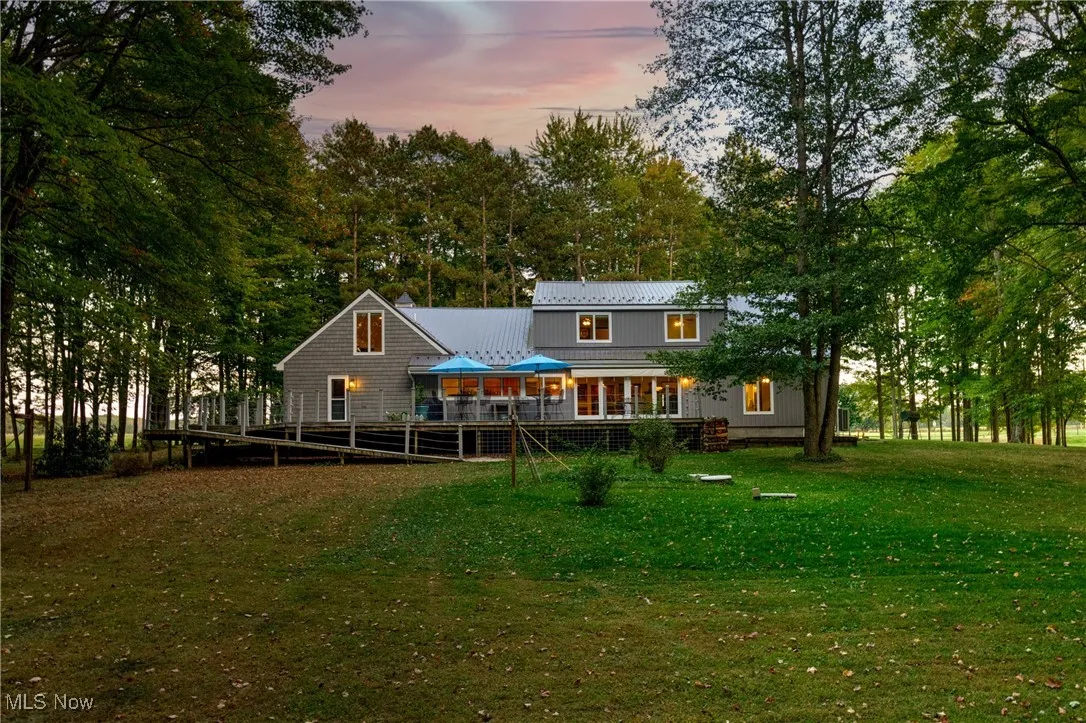 Back of property at dusk with a porch, a metal roof, a lawn, and view of scattered trees