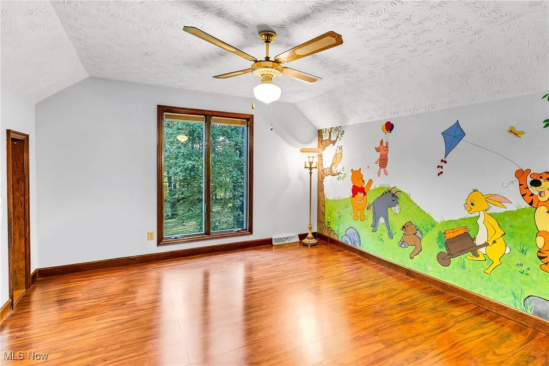 Additional living space with a textured ceiling, lofted ceiling, wood finished floors, and ceiling fan