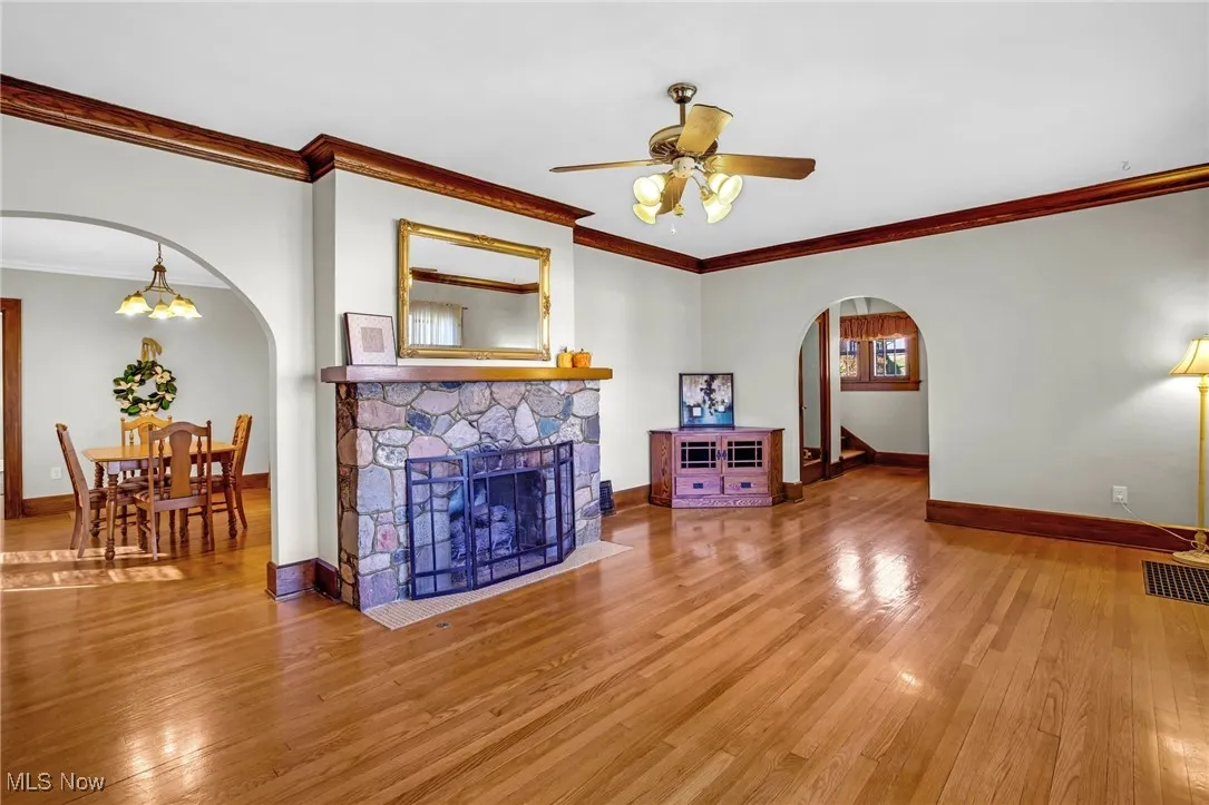 Living area featuring arched walkways, crown molding, wood-type flooring, and a fireplace