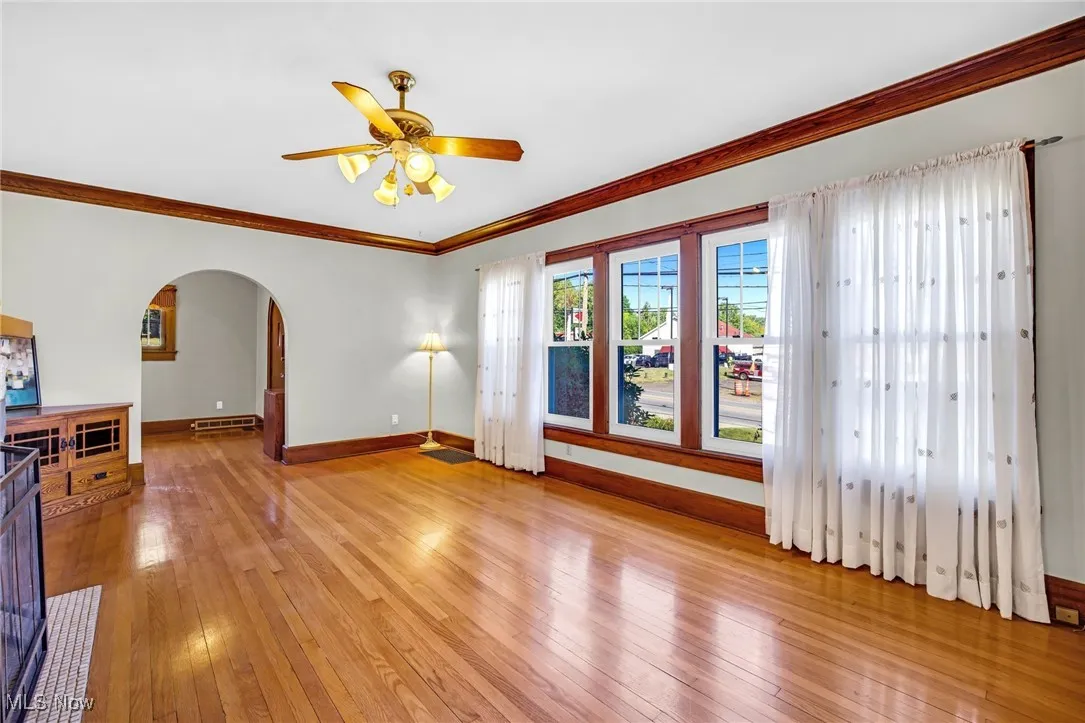 Unfurnished living room with crown molding, arched doorway , light wood finished floors, and ceiling fan
