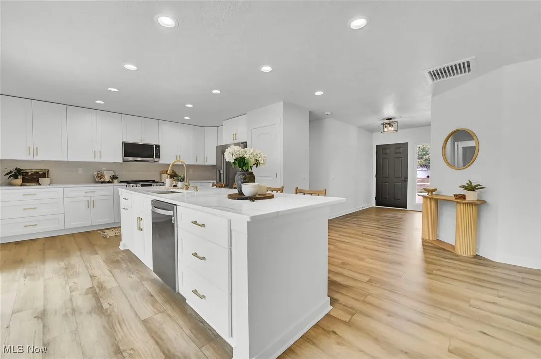 Kitchen with recessed lighting, a center island with sink, white cabinetry, light wood finished floors, and backsplash