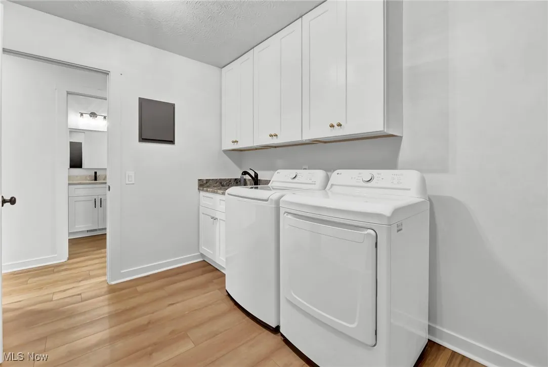 Laundry room with a textured ceiling, light wood finished floors, washing machine and clothes dryer, and cabinet space