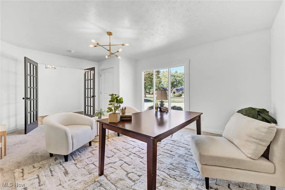 Carpeted office space featuring french doors, a chandelier, and a textured ceiling