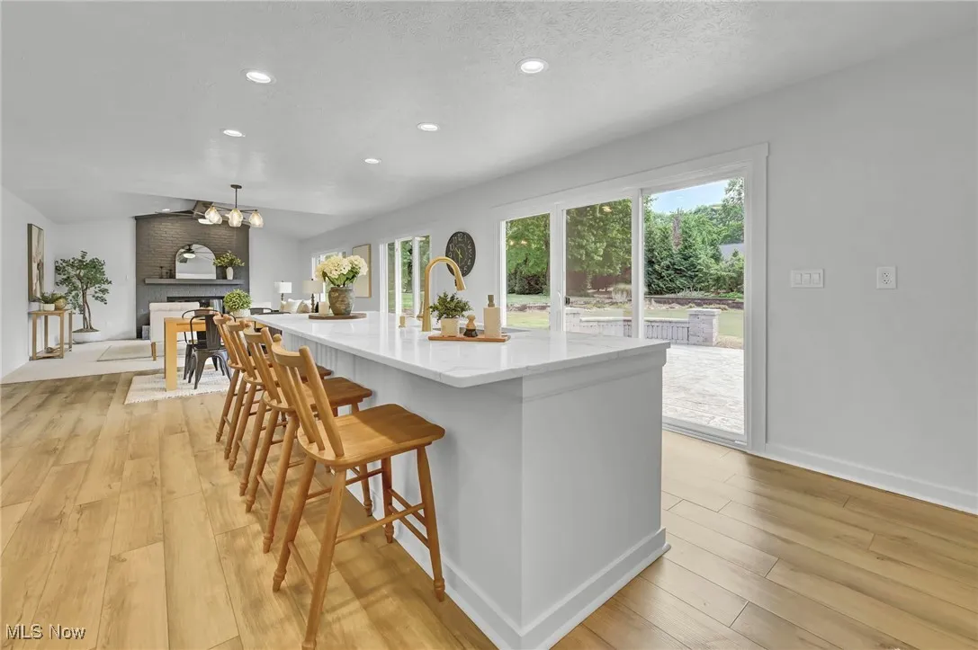 Kitchen with vaulted ceiling, plenty of natural light, light stone counters, a center island with sink, and recessed lighting
