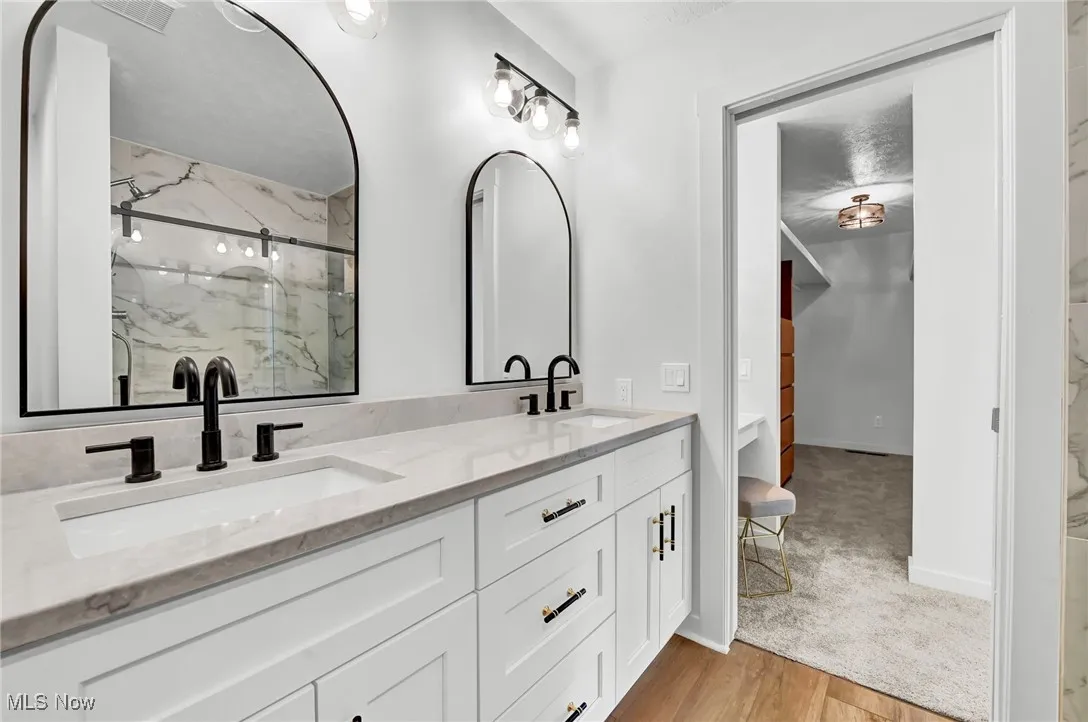 Bathroom featuring light wood-type flooring, a marble finish shower, and double vanity