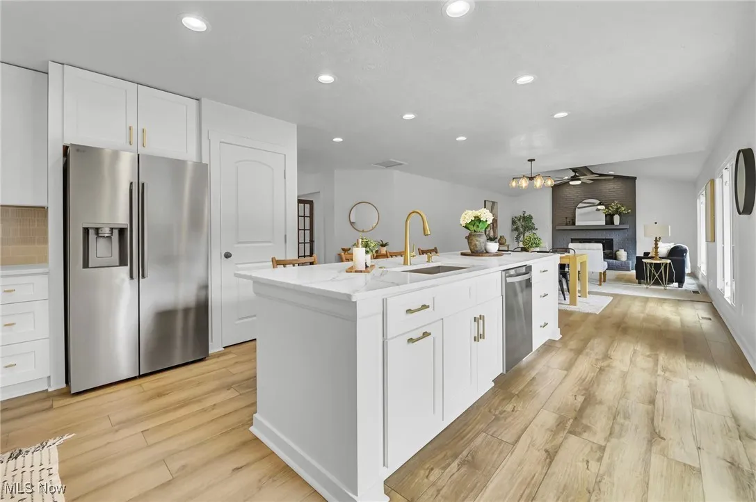 Kitchen with appliances with stainless steel finishes, white cabinetry, light wood-type flooring, a fireplace, and recessed lighting