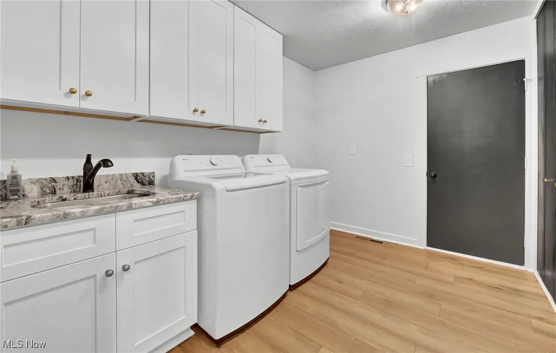 Washroom with a textured ceiling, light wood-style flooring, cabinet space, and washing machine and dryer