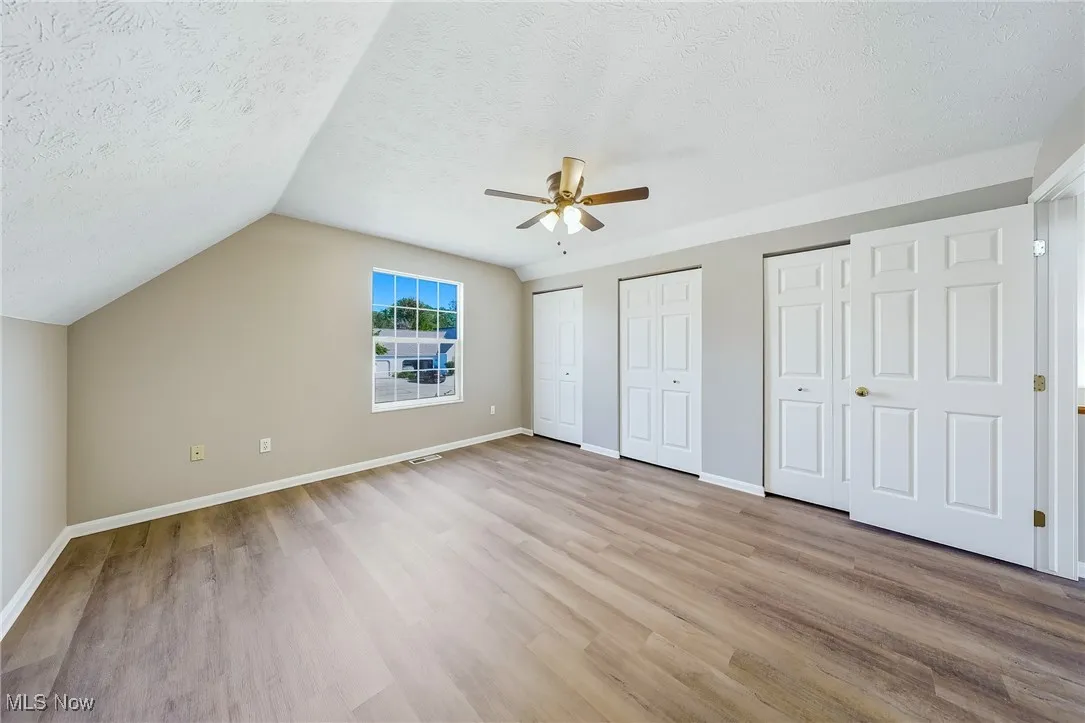 Unfurnished bedroom with two closets, light wood finished floors, lofted ceiling, a textured ceiling, and a ceiling fan