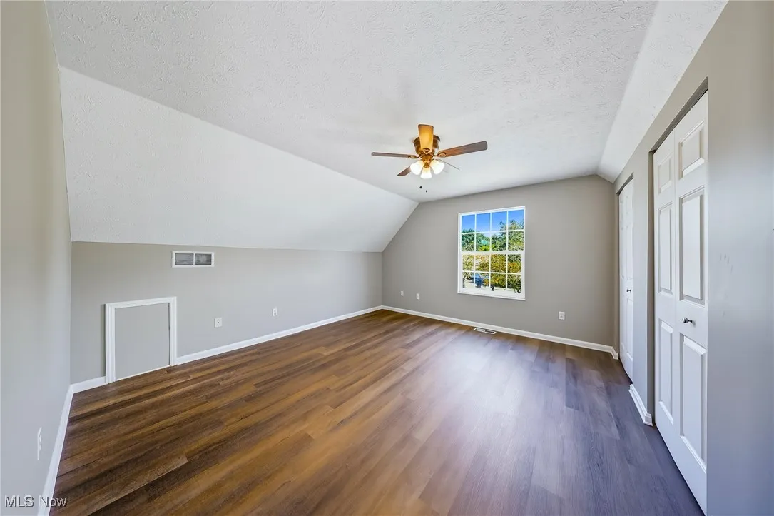 Additional living space with lofted ceiling, dark wood-style flooring, a textured ceiling, and ceiling fan
